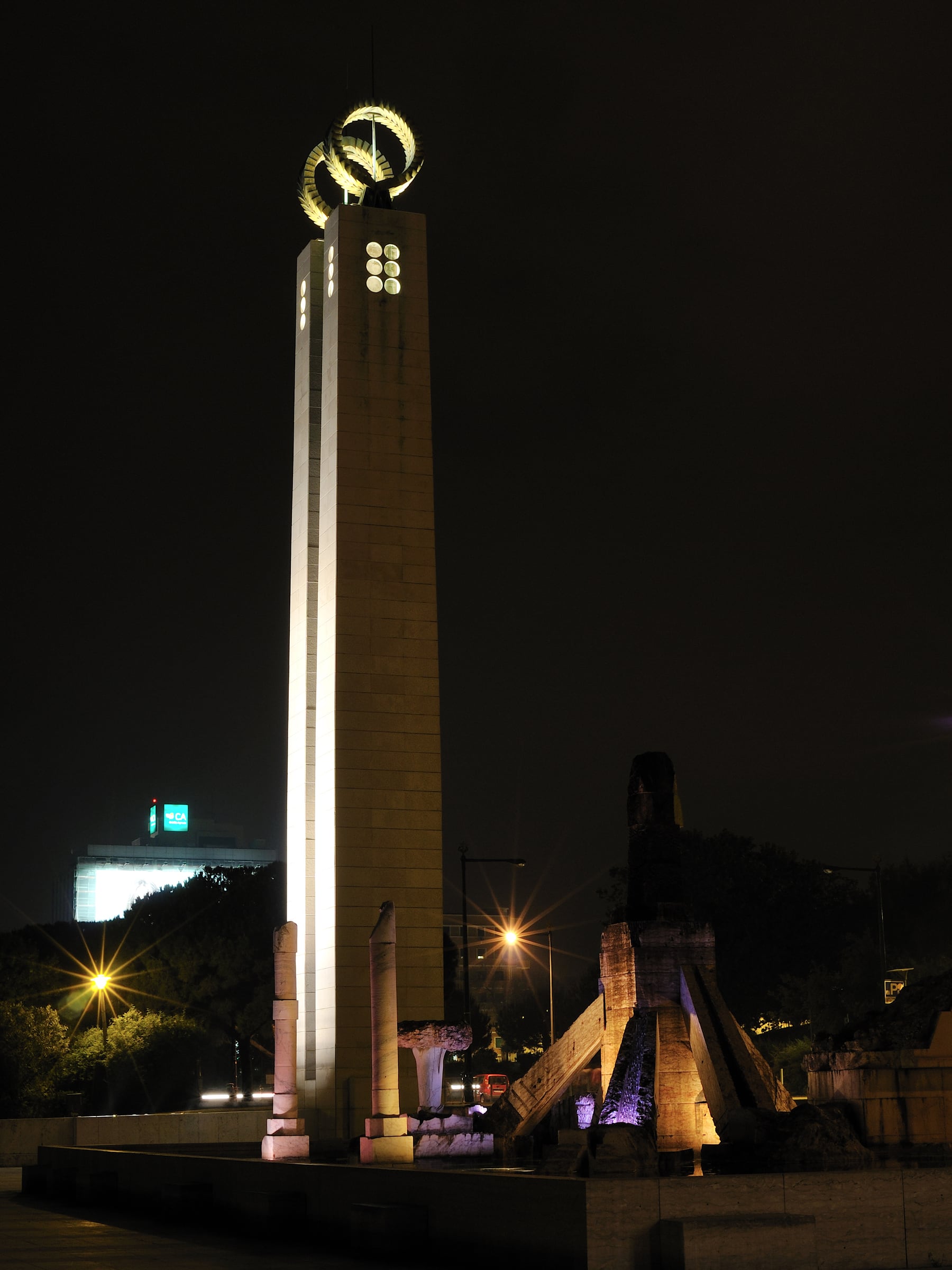 The column at Parque Eduardo VII lit from below over its full height, the ring at the top alight and the city dark around it.