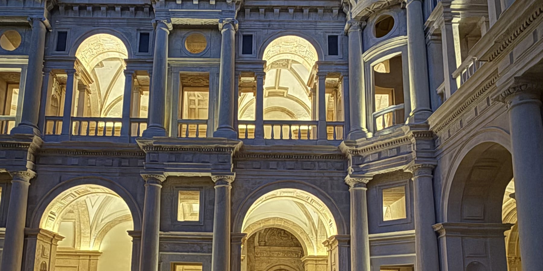The Claustro de Dom João III at the Convento de Cristo at blue hour, the arcades of both storeys washed with warm light under a sky still blue.
