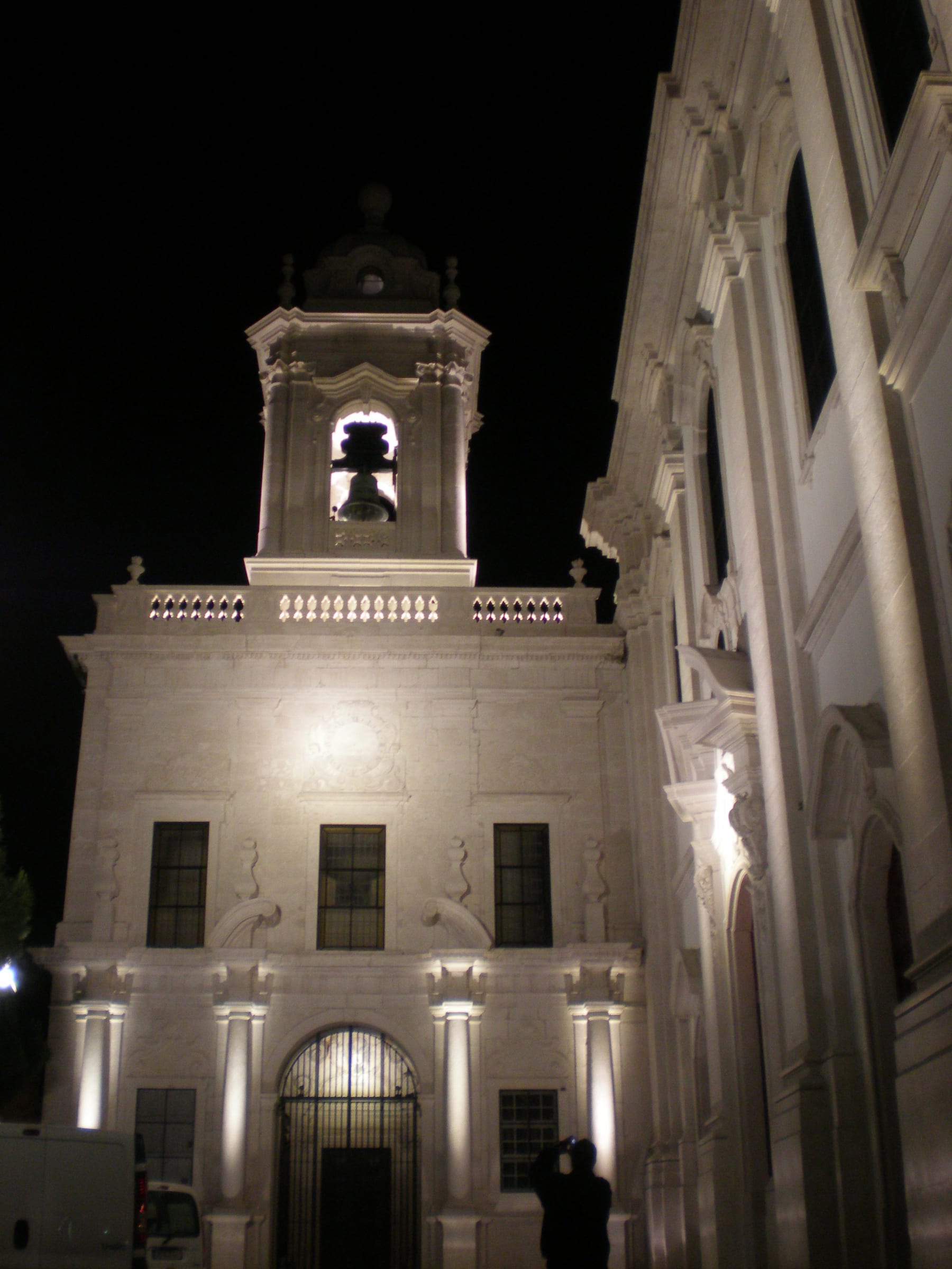 The front of the Graça church lit at night, the belfry alight above the balustrade and the stone washed from below down to the portal.