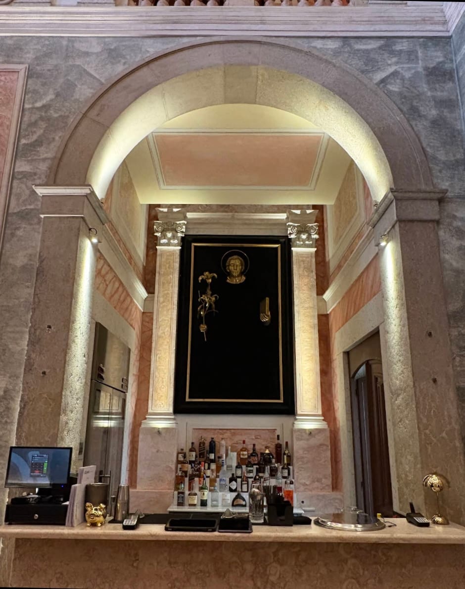 The àcapela bar counter under the chancel arch, the pilasters and the vault washed from below and, beyond it, Carlos Aires's black and gold panel above the bottle shelf.