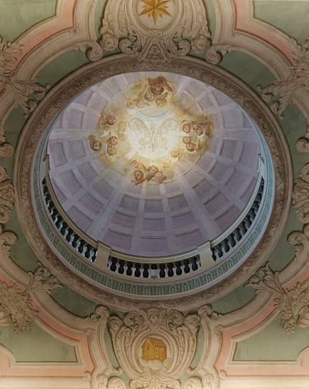 The chapel dome seen straight up, its coffers rising to the lantern and painted angels ringing the light.
