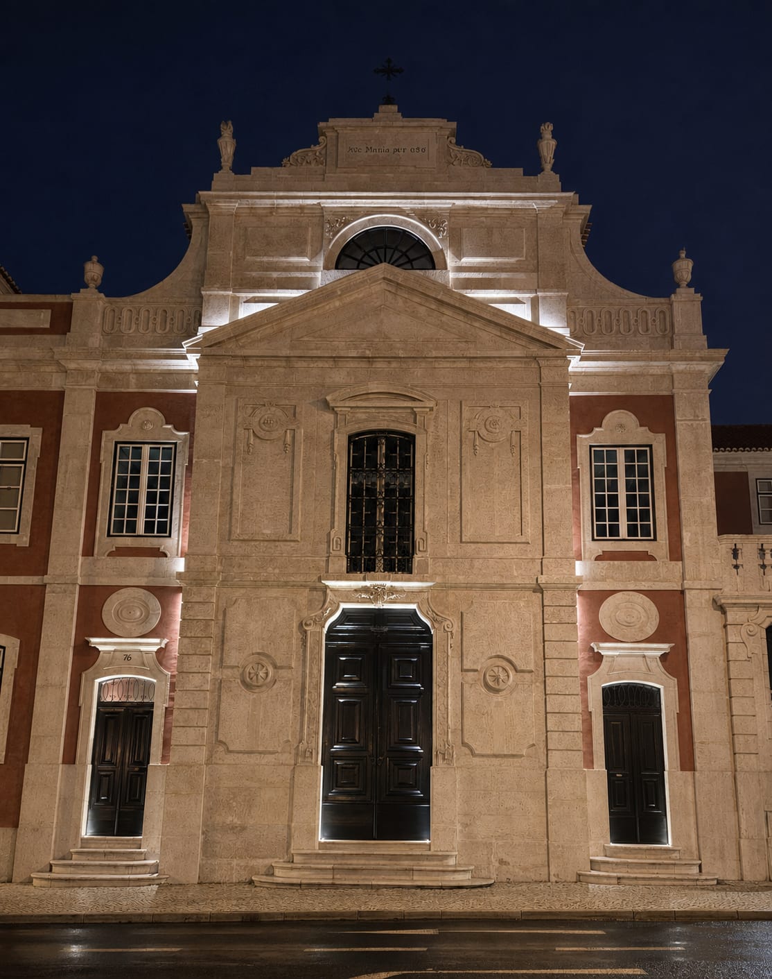 The palace church facade at night, grazed from below, the quoins, the pediment and the door surrounds drawn in light against the deep blue sky.