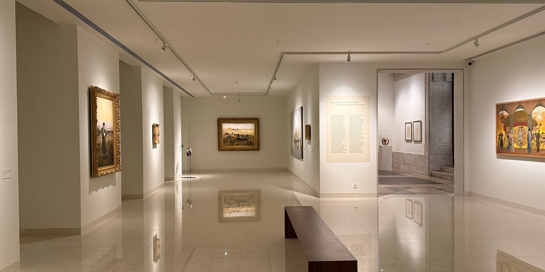 The enfilade of galleries, each painting taken by its own spot and the mirrored floor doubling the sequence to the far end.