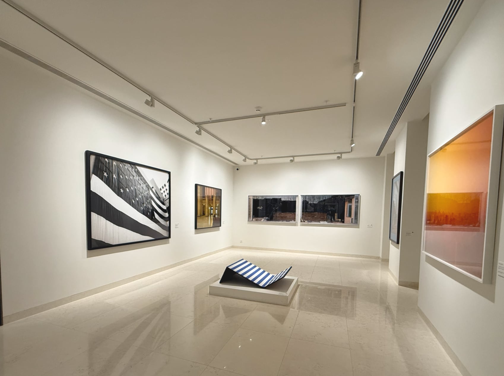 The photography room, the tracks drawing the route across the ceiling and every print taken without a reflection in its glass; the striped chaise on its plinth at the centre.