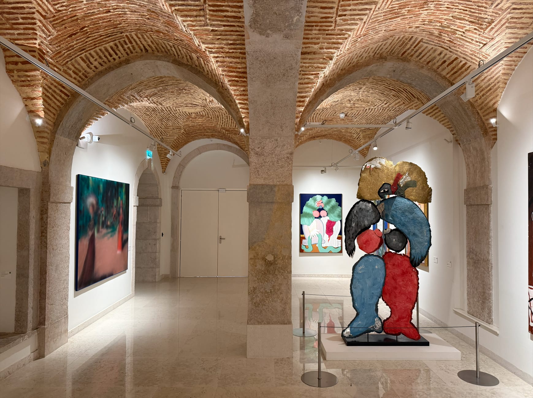 A contemporary art gallery under the brick vaults, the sculpture at the centre.