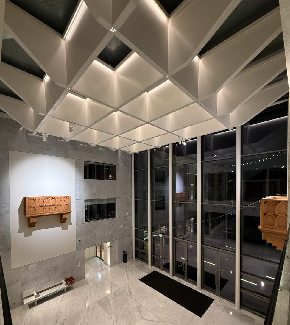 The entrance atrium under its faceted ceiling, the light caught in the folds and the glazed facade at night.