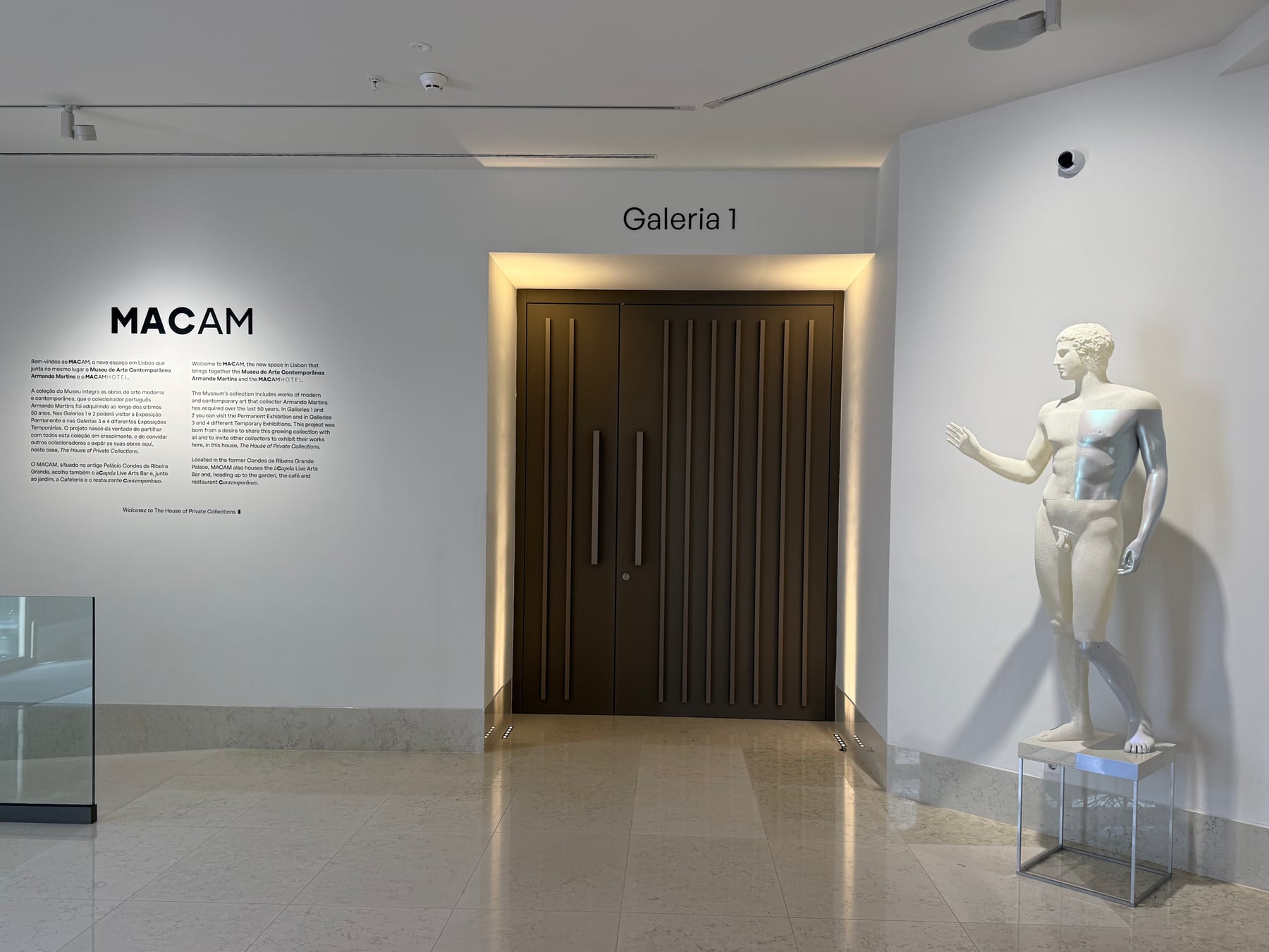 The entrance to Gallery 1, the wall text washed by a cove, the timber door at the centre and the classical sculpture lit inside its case.
