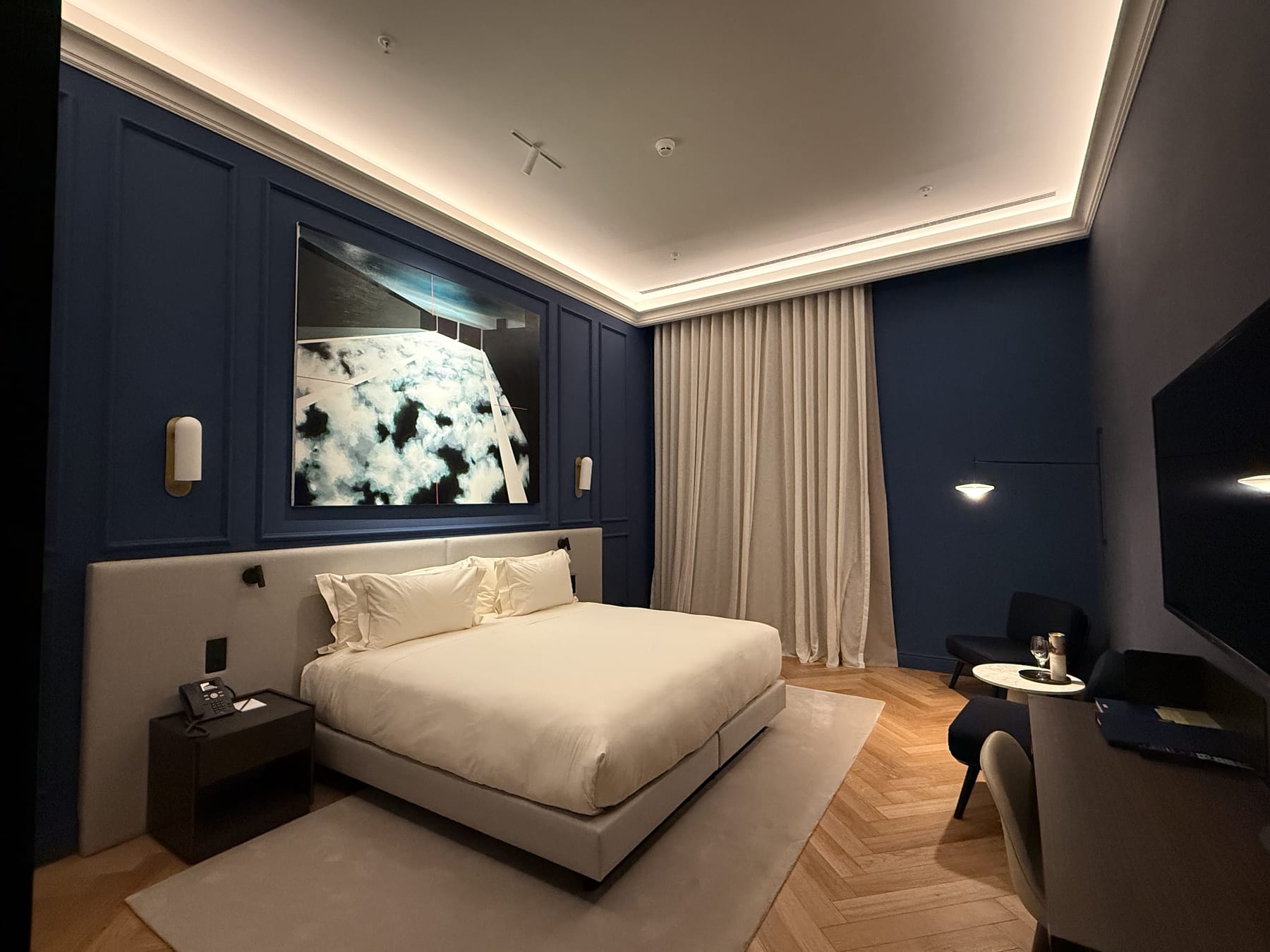 A room in deep blue, the cove separating the pale ceiling from the dark walls and wall lights flanking the painting.