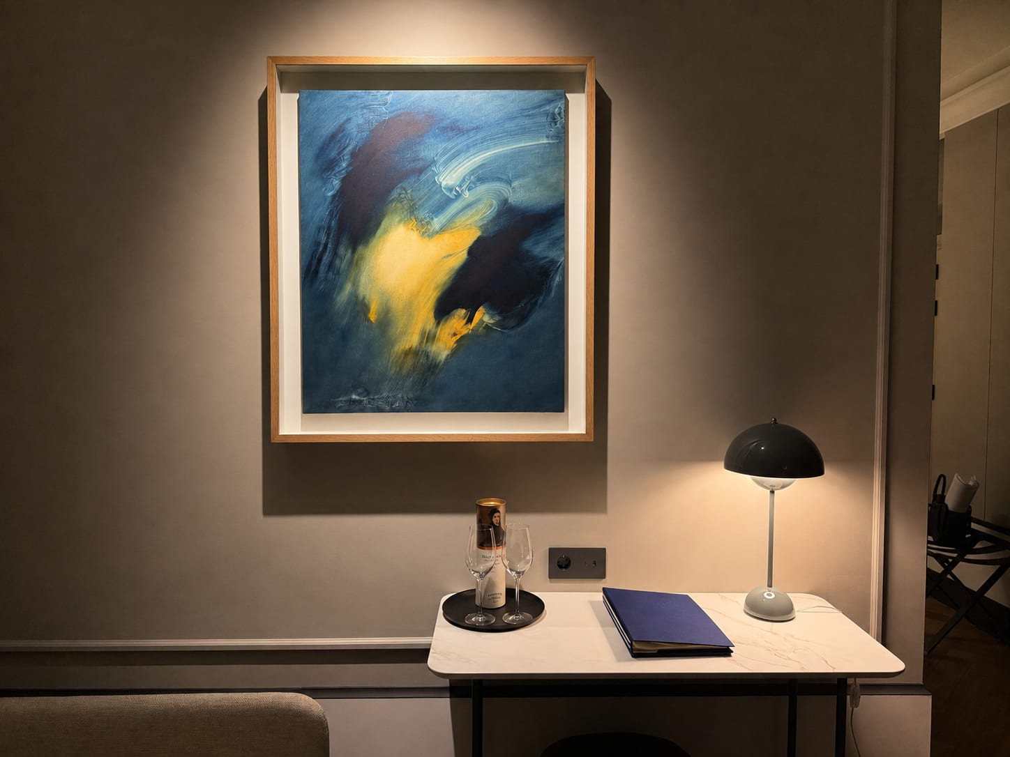 A painting on a narrow beam above the marble desk, the table lamp making the second layer.