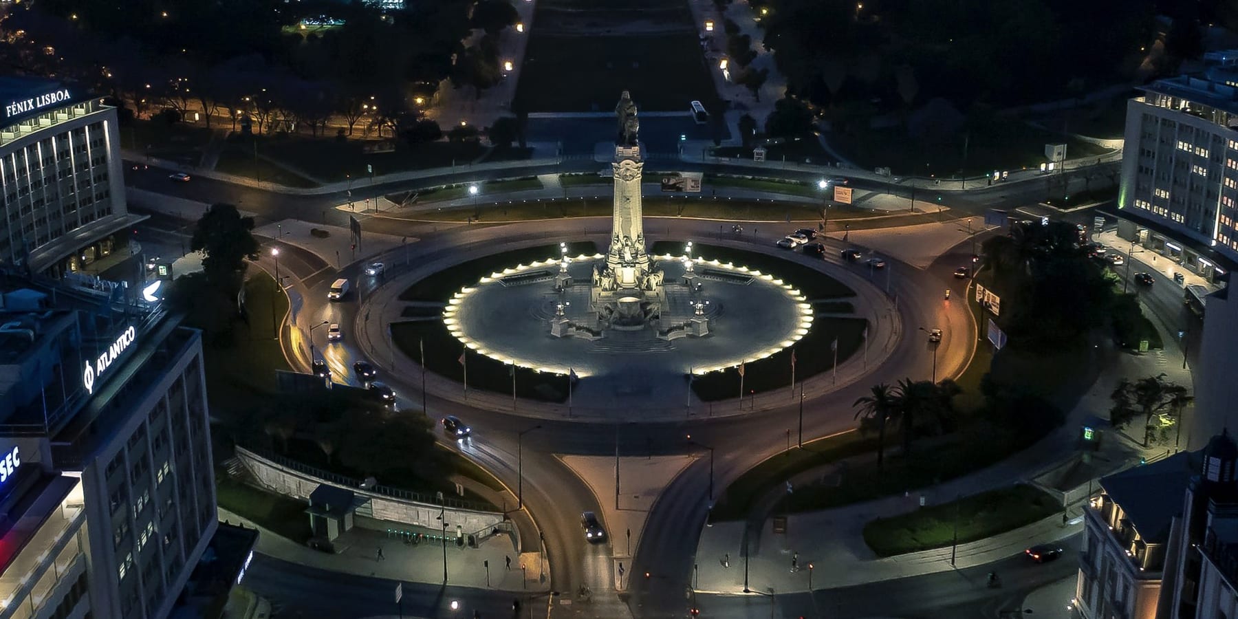 Aerial view of the Marquês de Pombal roundabout in Lisbon at dusk, the ring of light drawing the garden around the monument and the Avenida da Liberdade running away below. Urban lighting design by Diana Delnegro Architectural Lighting.