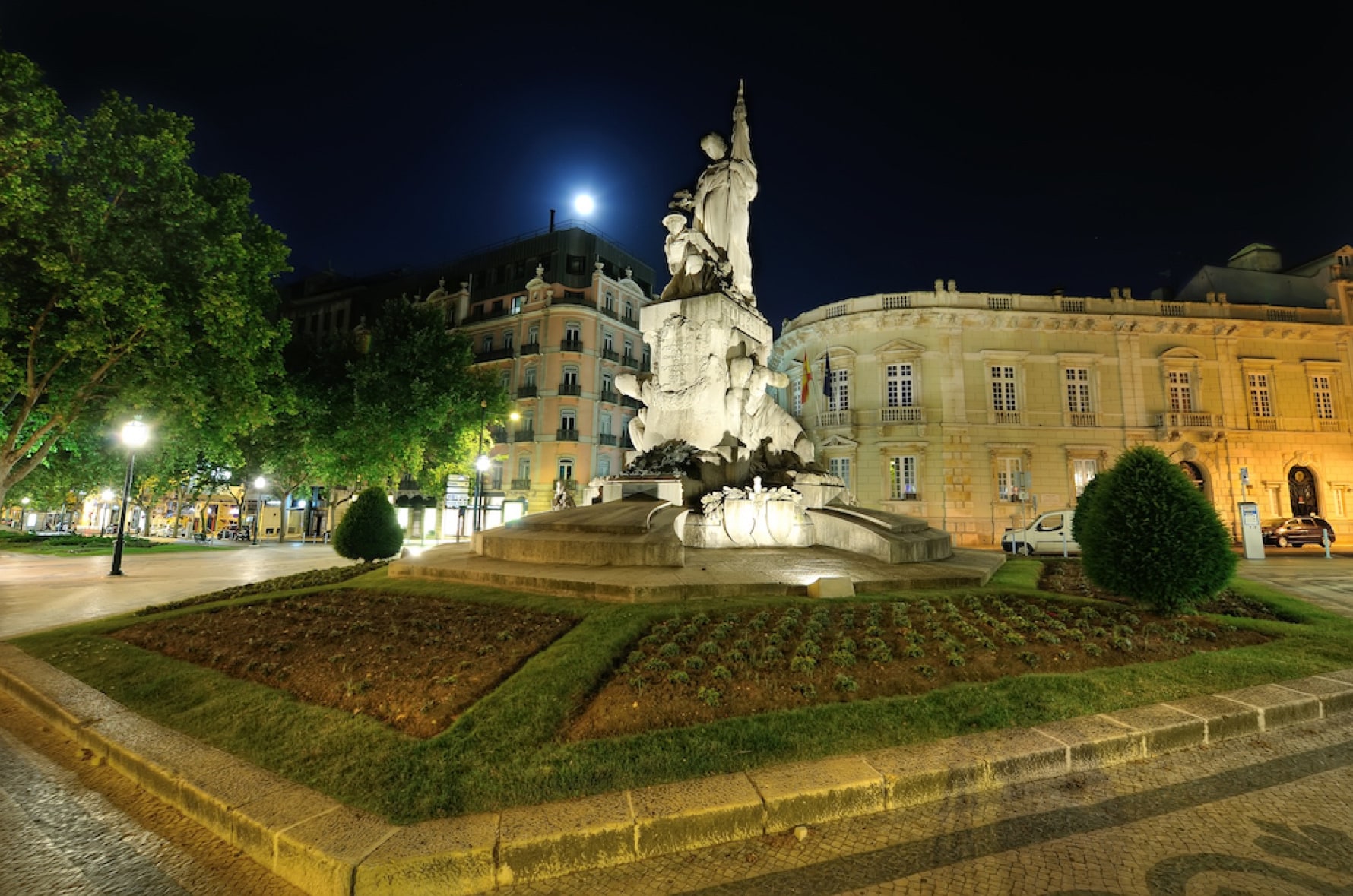 The Monument to the Dead of the Great War lit at the centre of its bed, the bronze figure taking light from below and the Avenida facades behind.