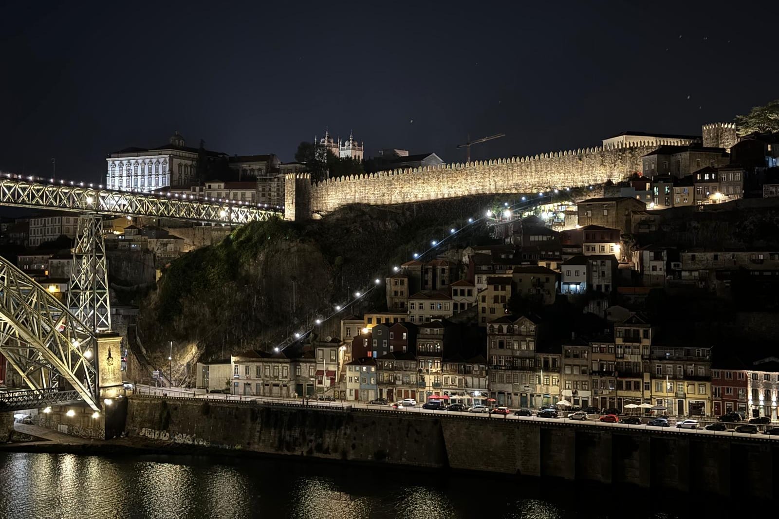 A mesma vista depois da intervenção: a muralha corre iluminada ao longo de toda a crista, acima do casario da Ribeira, com as ameias legíveis da outra margem.